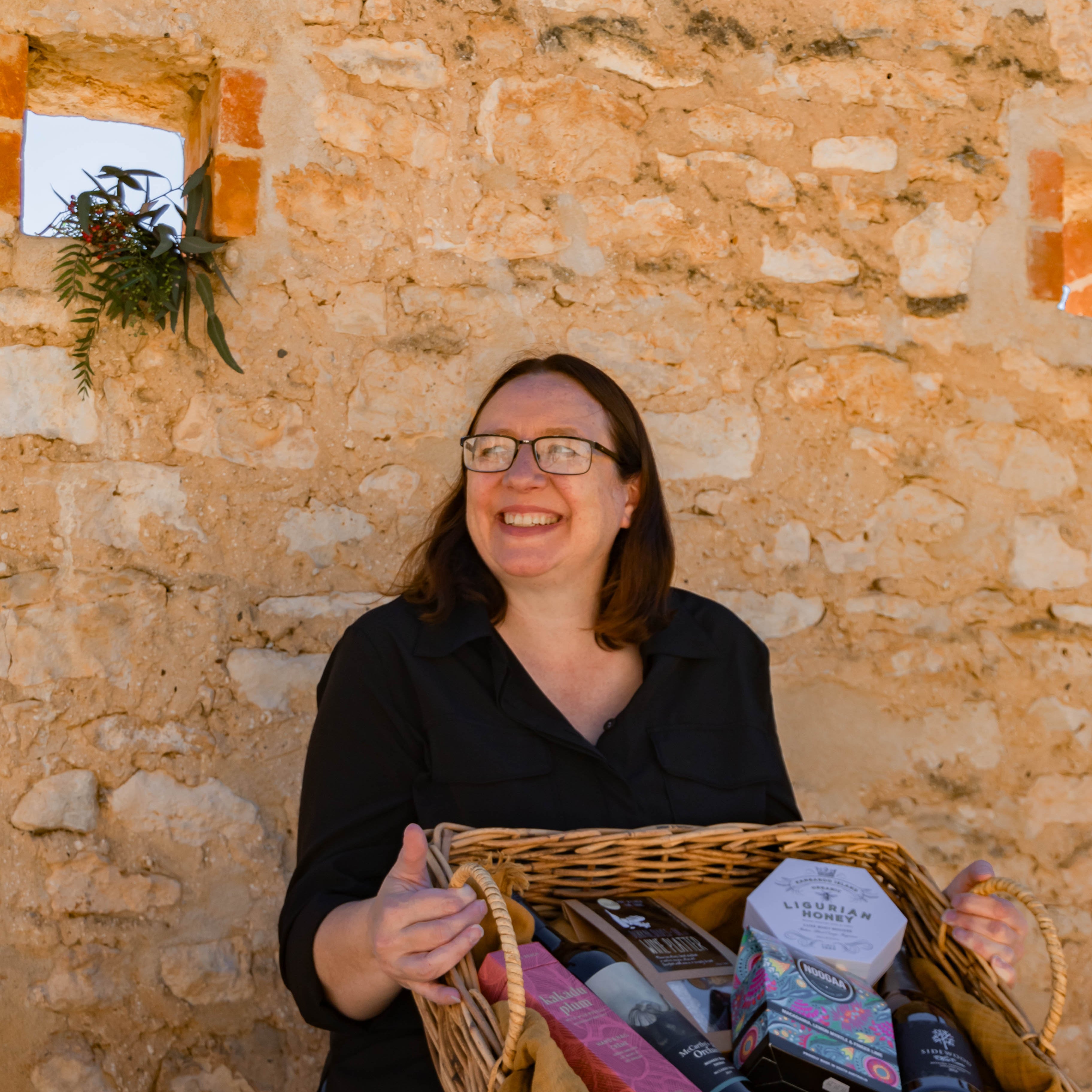 Woman holding a woven basket with items against a stone wall.