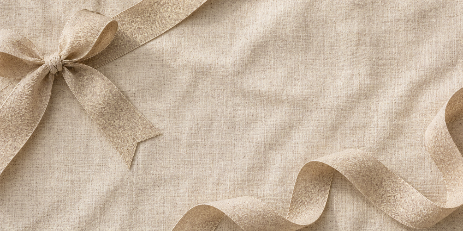 A close-up of a light beige fabric surface with a matching ribbon bow on the left and a flowing ribbon tail at the bottom right.